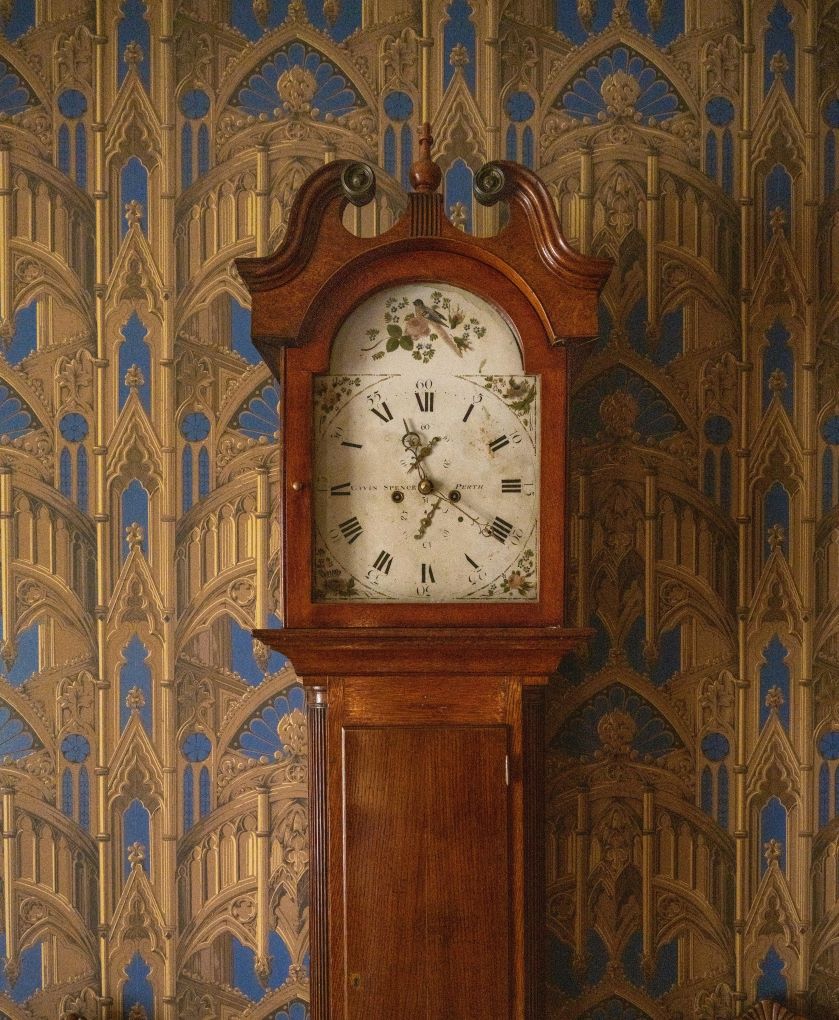 Wooden antiqe clock in front of wall with wallpaper